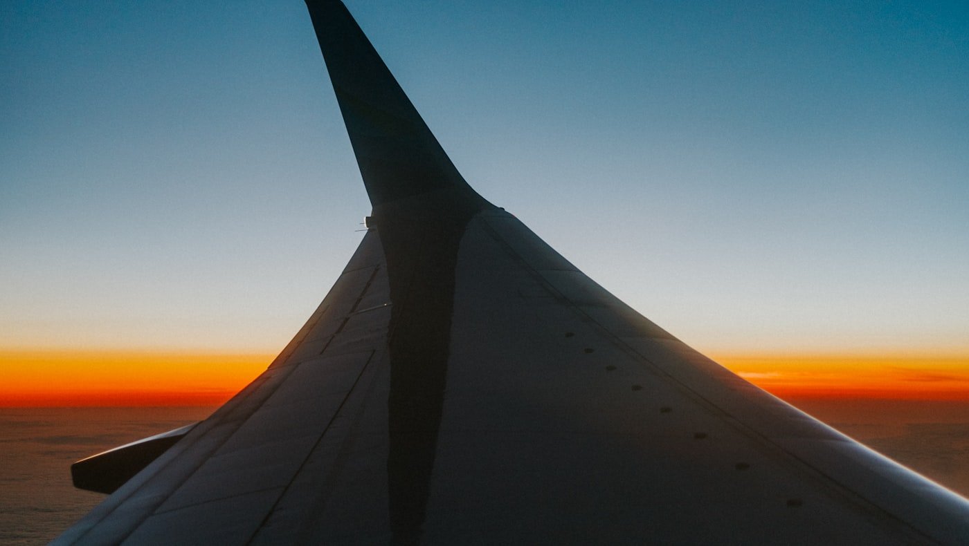 Asa de avião com o pôr do sol no horizonte durante voo internacional